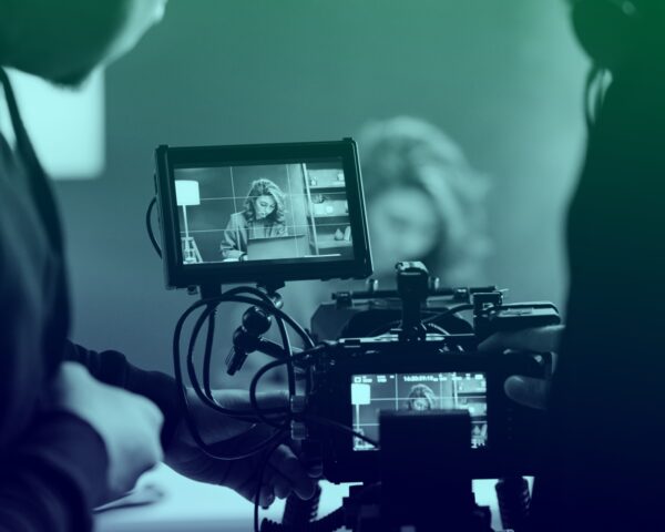 Photo of a video camera filming a scene in the background. We are looking into the camera as if we are operating it, and the background scene is slightly out of focus.
